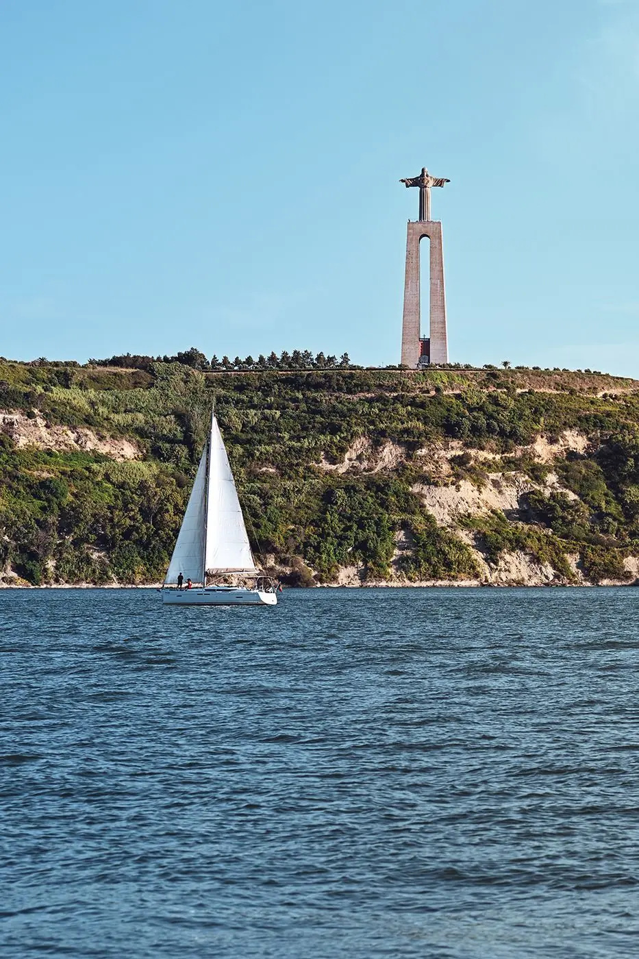 Sailboat crossing the Tagus River beneath the Cristo Rei statue, Lisbon
